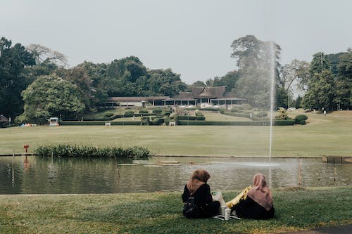 Women Wearing Headscarves Sitting by a Pond in a Park
