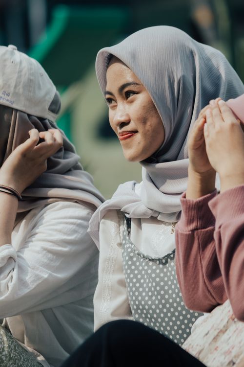 Free A joyful moment of an Asian woman in a headscarf smiling outdoors with friends. Stock Photo
