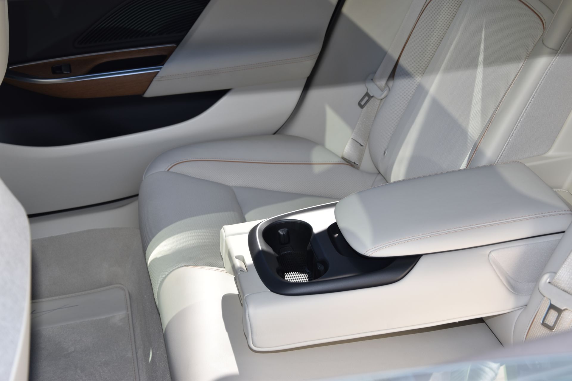 Elegant white leather car interior showcasing luxury and comfort with armrest and cup holder.