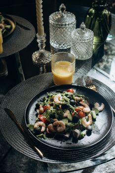 Elegant shrimp salad with cherry tomatoes and fresh greens paired with orange juice, set on a dining table.