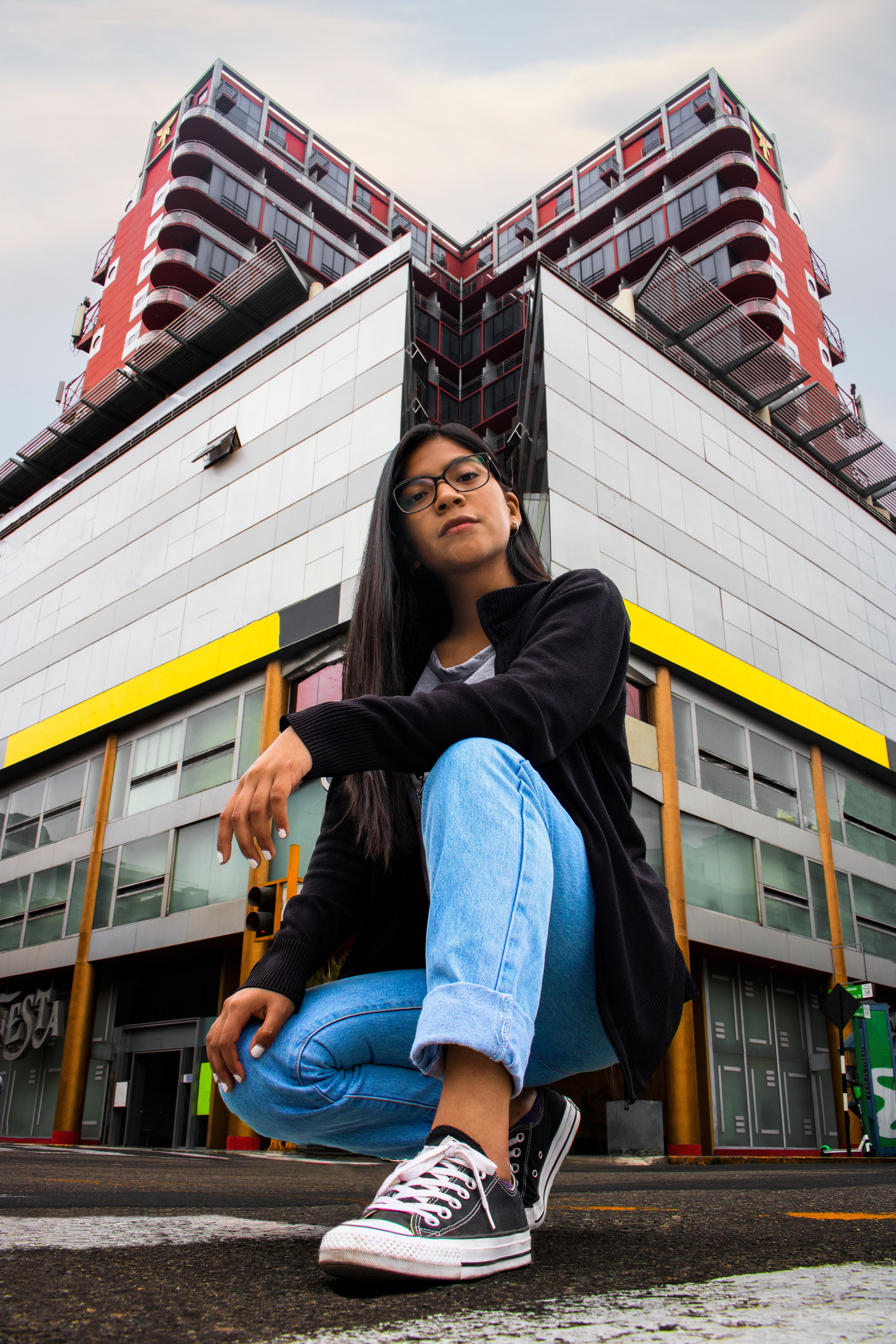 Young woman in urban setting with a striking building backdrop, showcasing modern fashion.