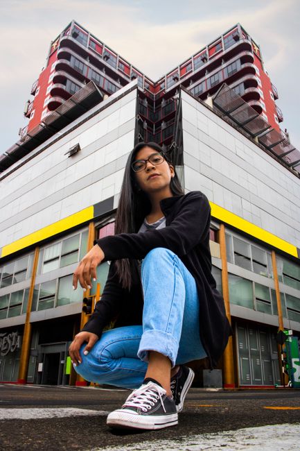 Young woman in urban setting with a striking building backdrop, showcasing modern fashion.