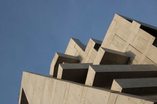 Free A low angle shot of a modern concrete building with geometric layers against a clear blue sky. Stock Photo