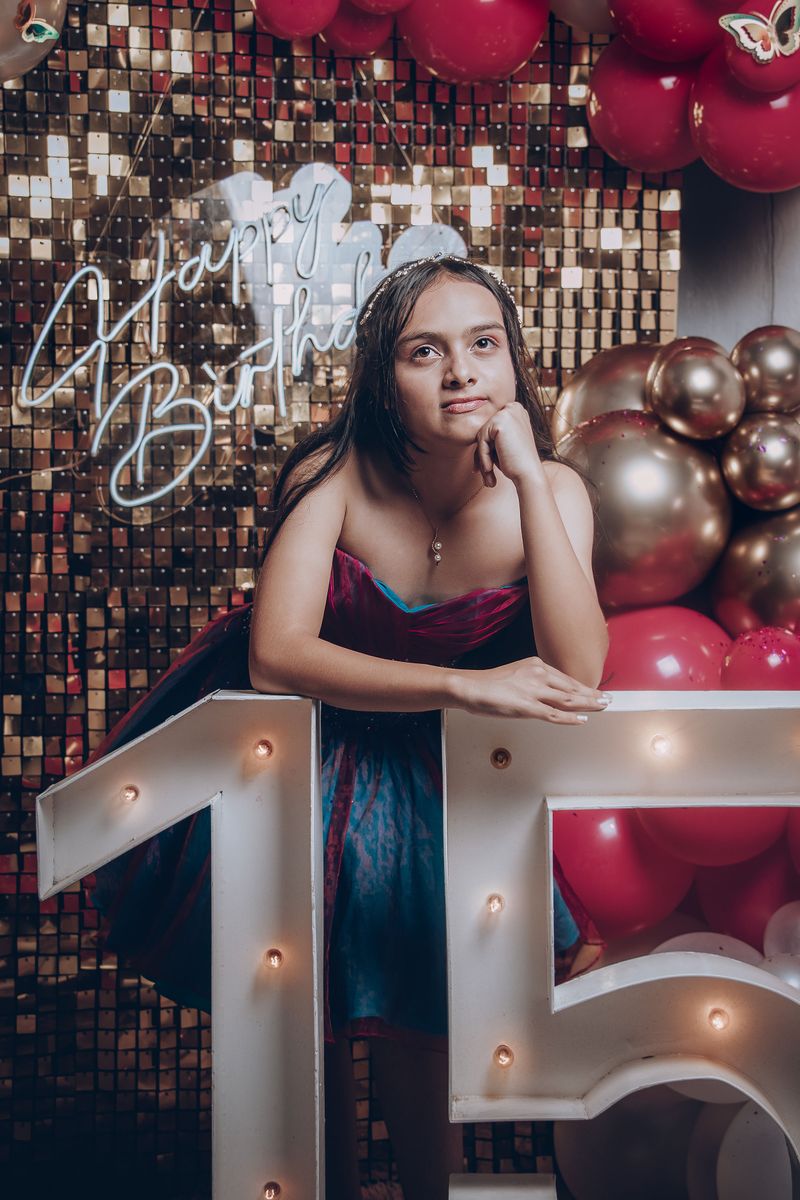 Girl standing among balloon and floral decorations set up for her fifteenth birthday party