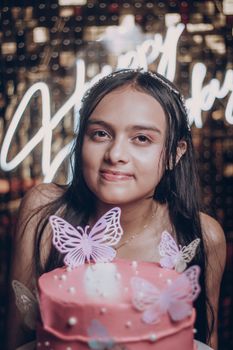 Teen girl celebrating birthday with pink cake adorned with butterflies in festive setting.
