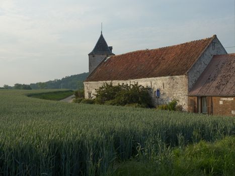 Charming stone church and farmhouse in lush green fields under a bright sky.