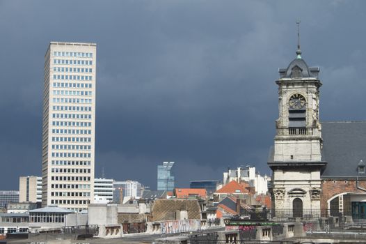 Dramatic view of Brussels showing a clock tower and modern skyscrapers under a dark sky.