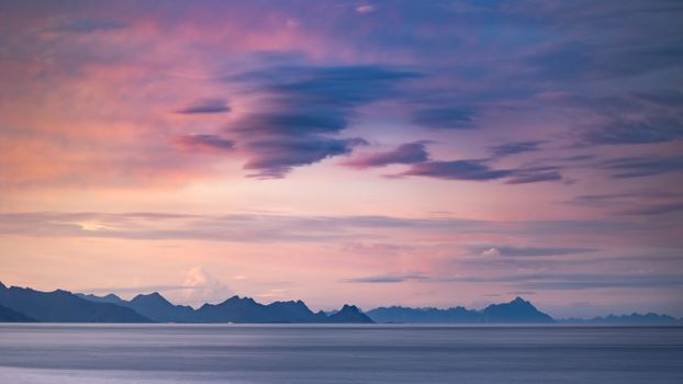 Stunning sunset over a mountain range with pink and purple sky reflections on wide open sea.