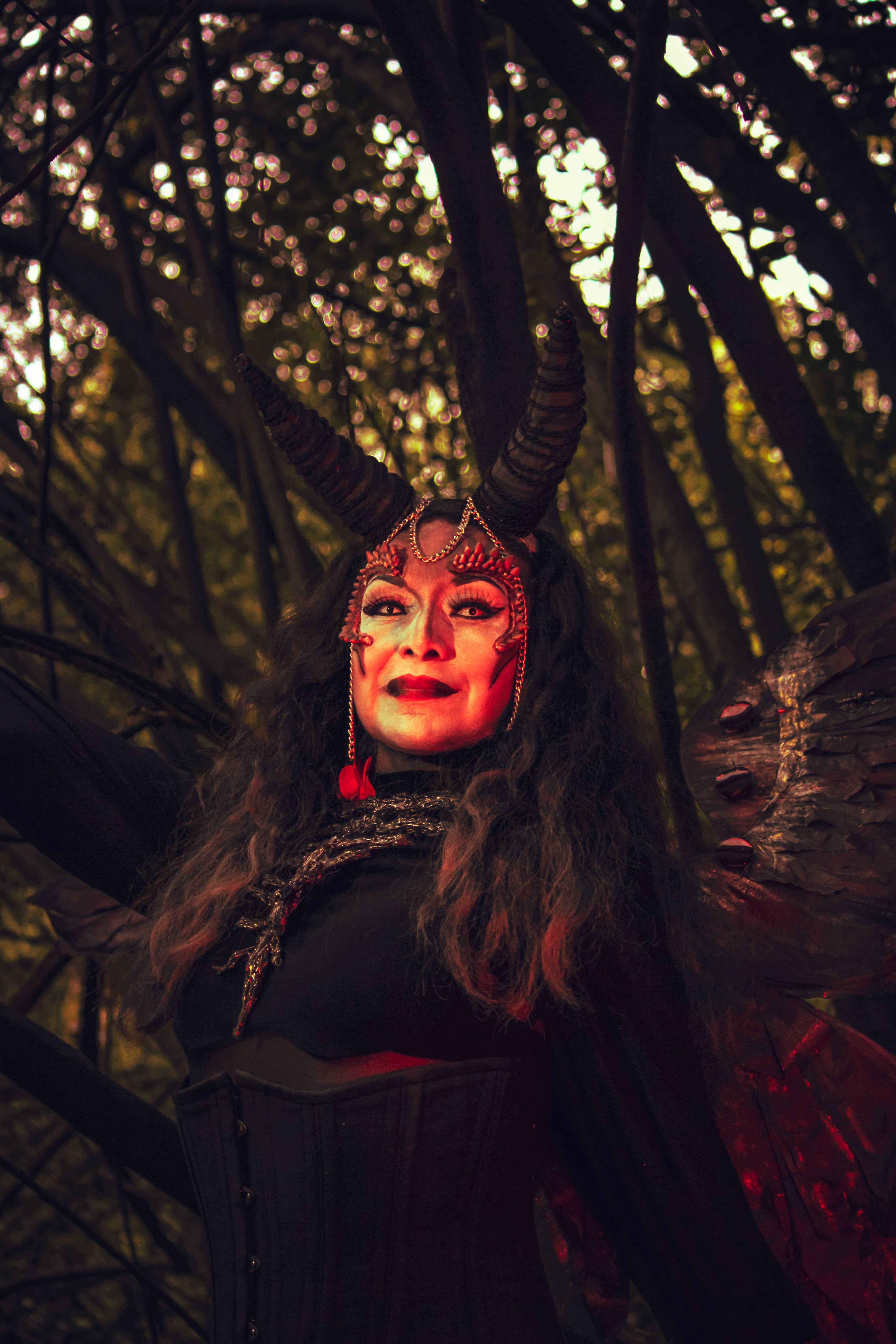 A captivating portrait of a woman in a devil costume with horns in a forest setting.