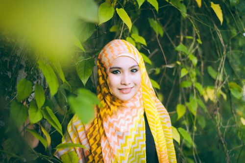 Free Smiling woman wearing a yellow headscarf surrounded by lush green leaves. Stock Photo
