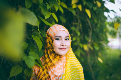 Free A young woman smiles warmly while wearing a vibrant headscarf among lush greenery. Stock Photo