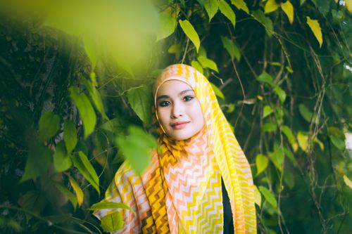 Free Portrait of a smiling woman wearing a vibrant headscarf, surrounded by lush greenery. Stock Photo