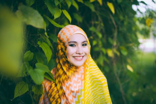 Free A young woman wearing a colorful hijab smiles joyfully amid lush green leaves. Stock Photo