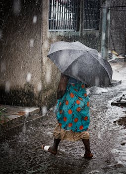 A woman with an umbrella walks through a rainy city street, highlighting urban life in harsh weather.