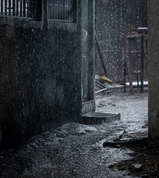 Atmospheric urban alley during heavy rain with reflections and dark tones.