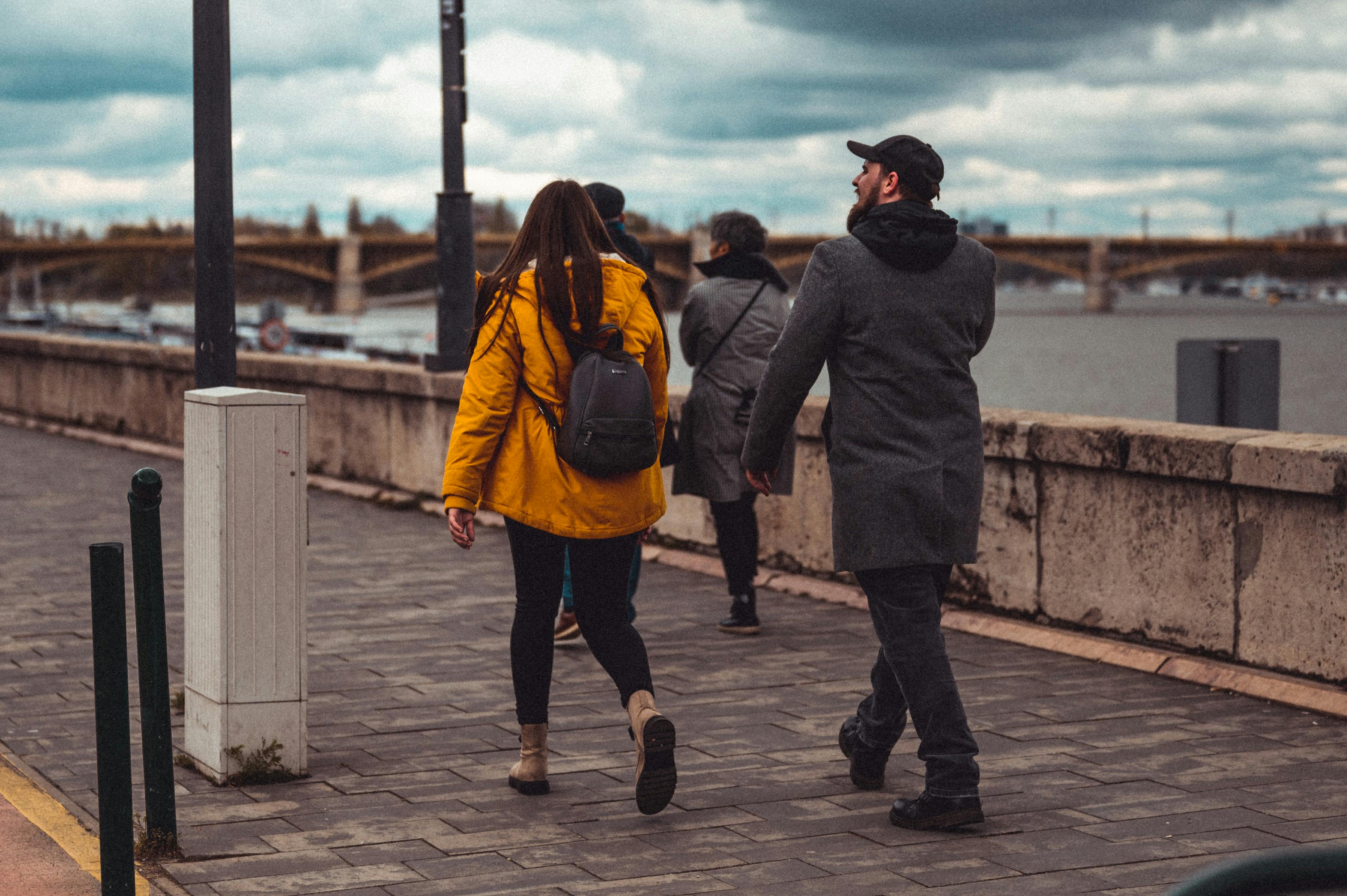 A couple strolling on a Budapest riverside promenade during a chilly fall day.