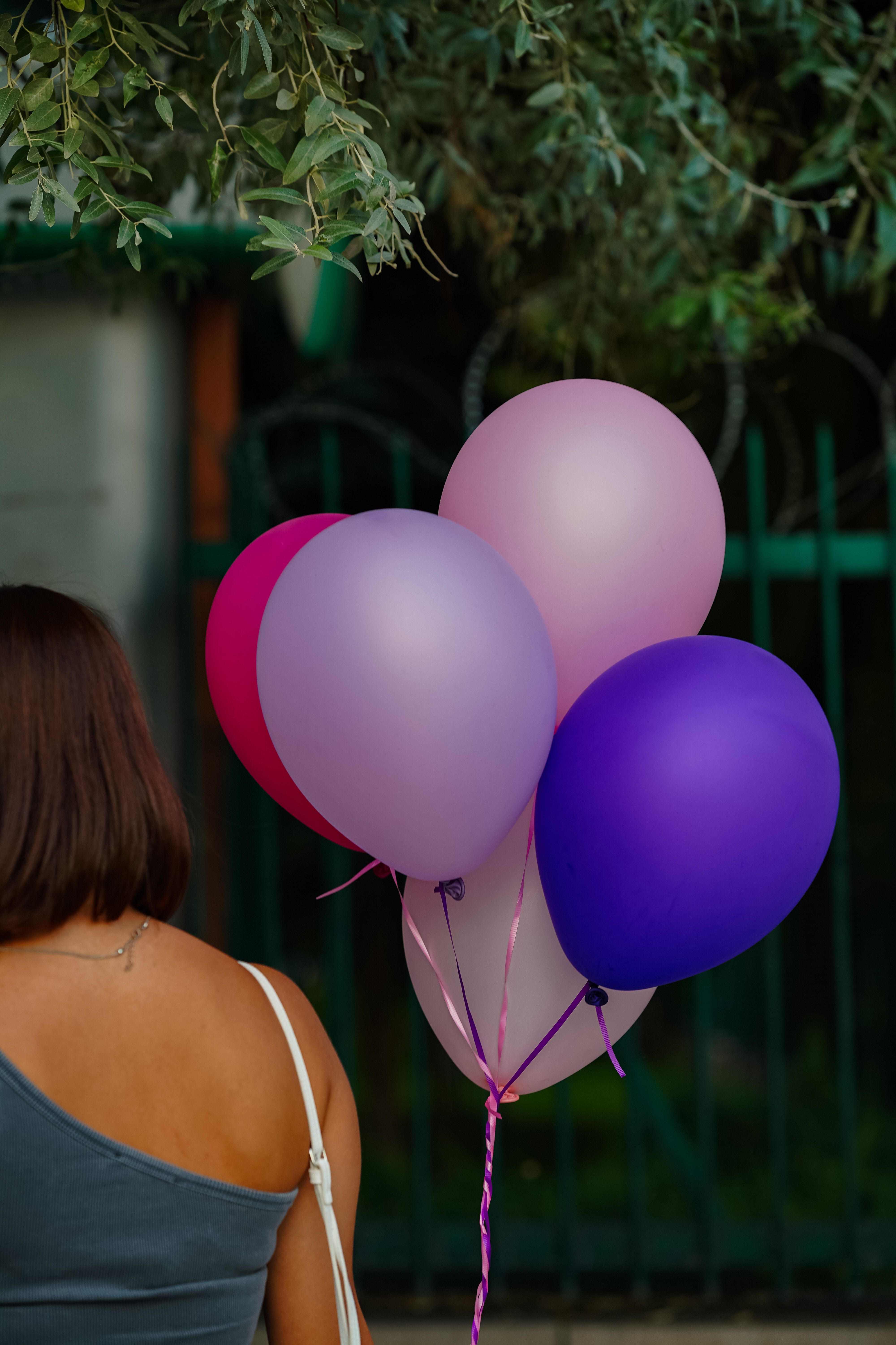 First birthday balloon decor ideas with woman holding pink and purple balloons at an outdoor garden party