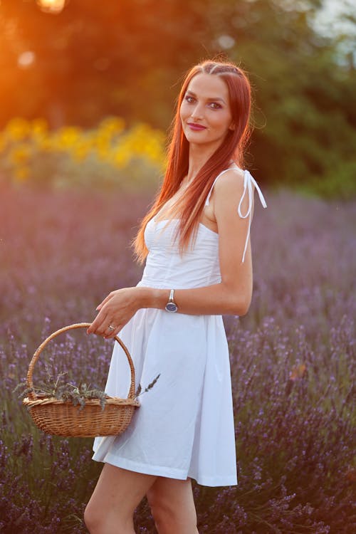Young Woman in White Strap Dress Posing in Lavender Field with a Wicker Basket