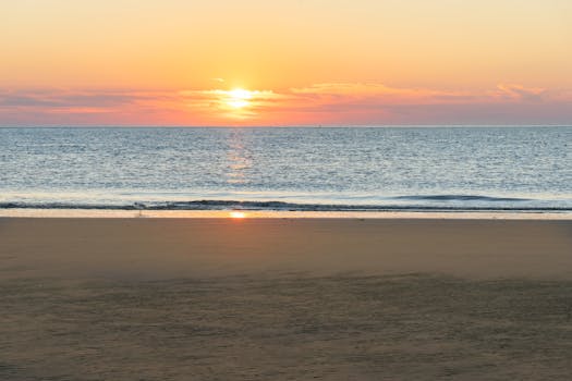 A tranquil beach scene during sunrise with gentle ocean waves under a vibrant sky.