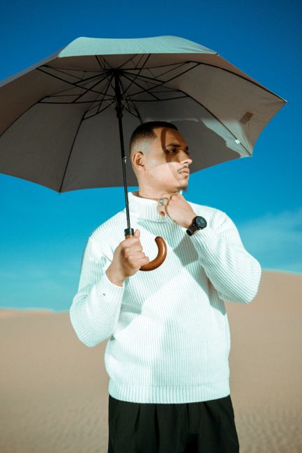 Portrait of a fashionable young man in a white sweater holding an umbrella in the desert.