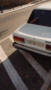 Vintage white Lada car parked on a sunlit urban street in Baku, Azerbaijan.