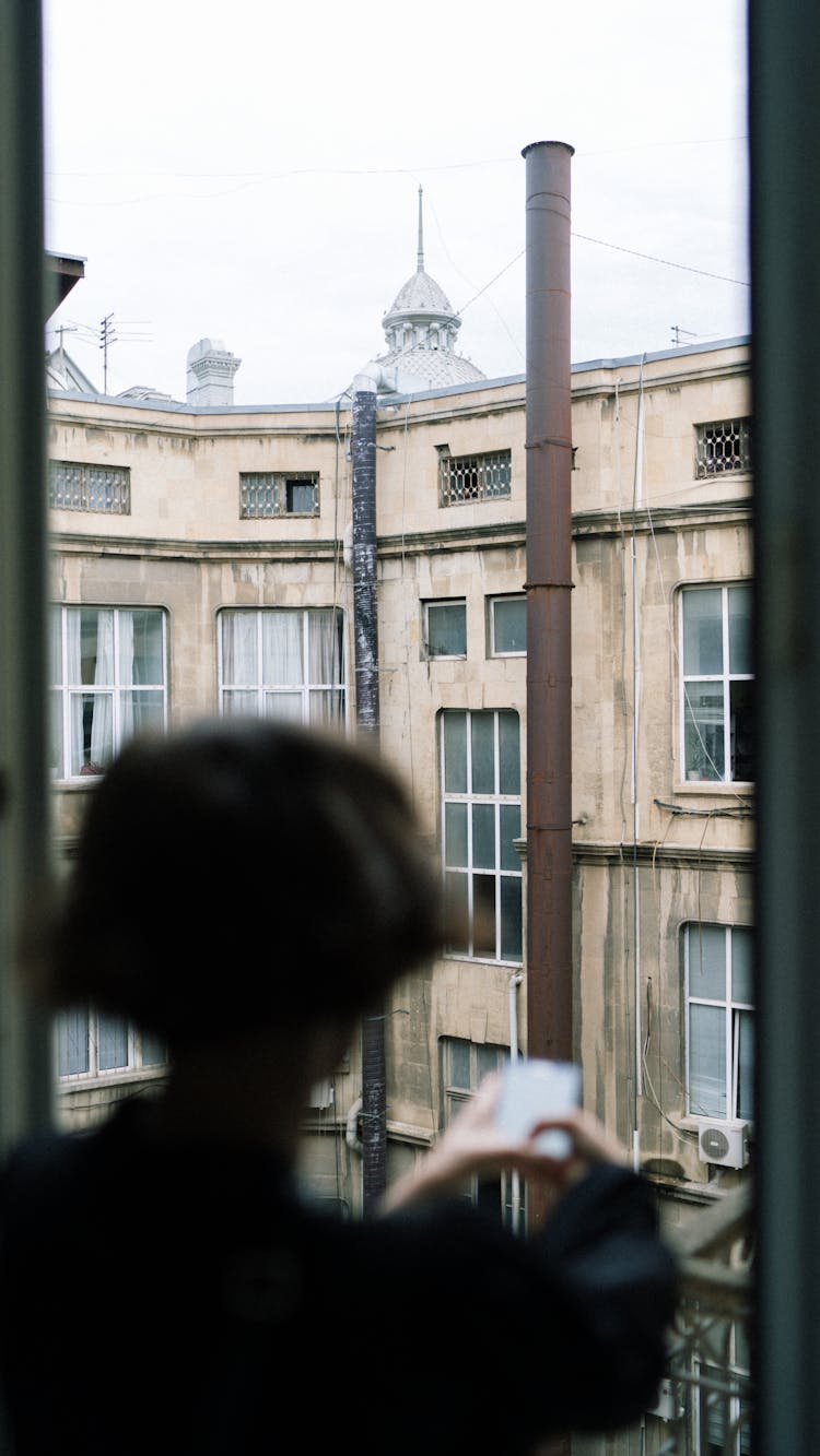 Silhouette Of A Resident In The Window Of The Top Floor Of An Apartment Building