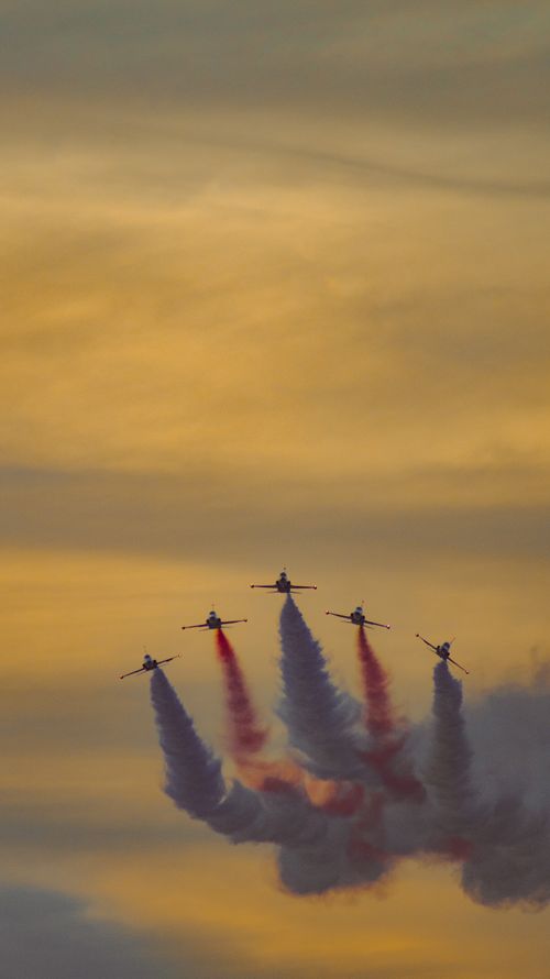 Free Five airplanes perform a stunning air show with smoke trails against a sunset sky. Stock Photo