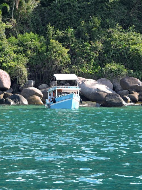 Free A small boat docked near rocky shore with lush greenery in the background, captured on a sunny day. Stock Photo