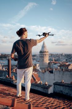 Man operating a drone on a rooftop with Galata Tower in Istanbul's skyline during the day.