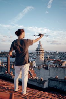 A young man controlling a drone with the historic Galata Tower in the background, Istanbul skyline.