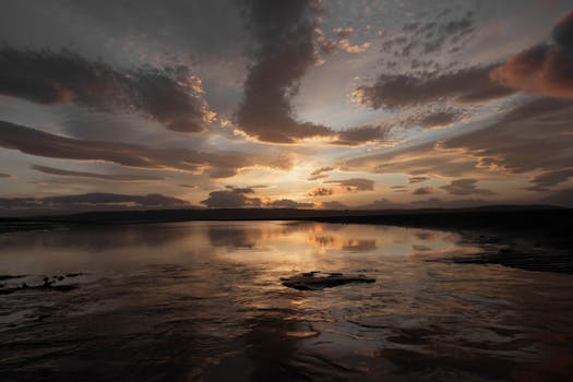 A breathtaking sunset reflecting over a serene lake with a dramatic sky and calm waters.