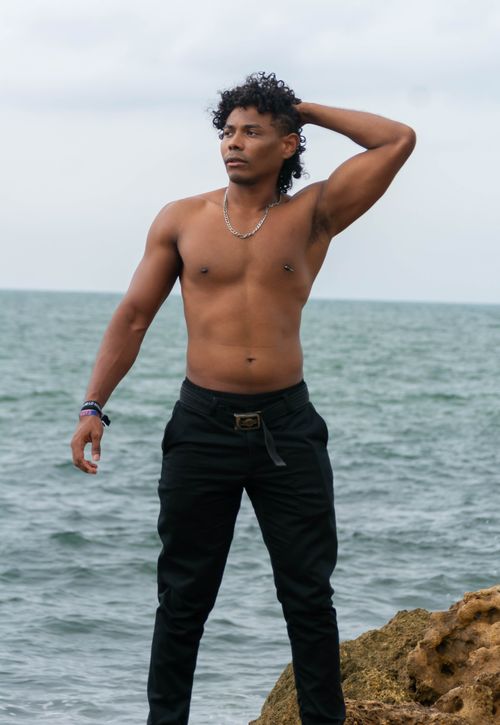 Free Shirtless man poses confidently by the ocean, displaying style and strength. Stock Photo