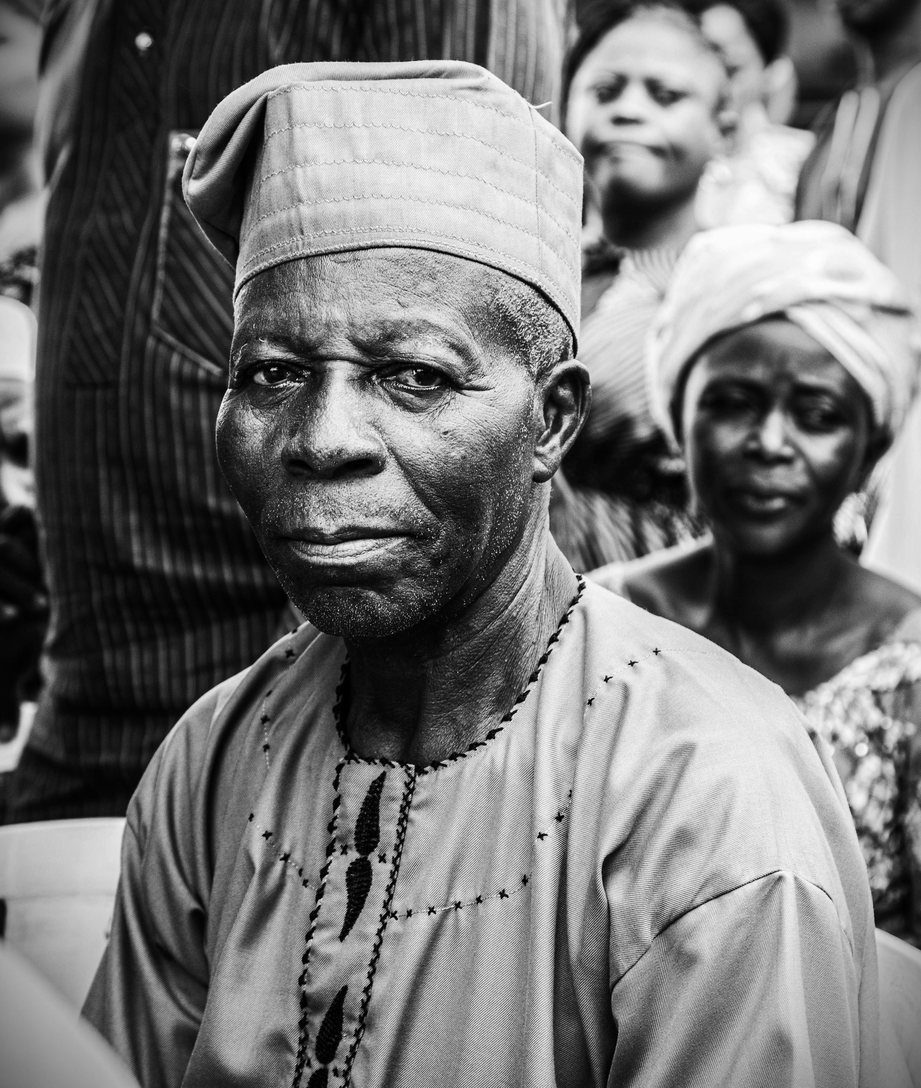 Black and white portrait of a traditional African man wearing a kufi in a rural setting.