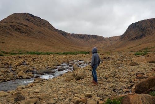 Person in Hoodie Standing on Rocks Near Stream