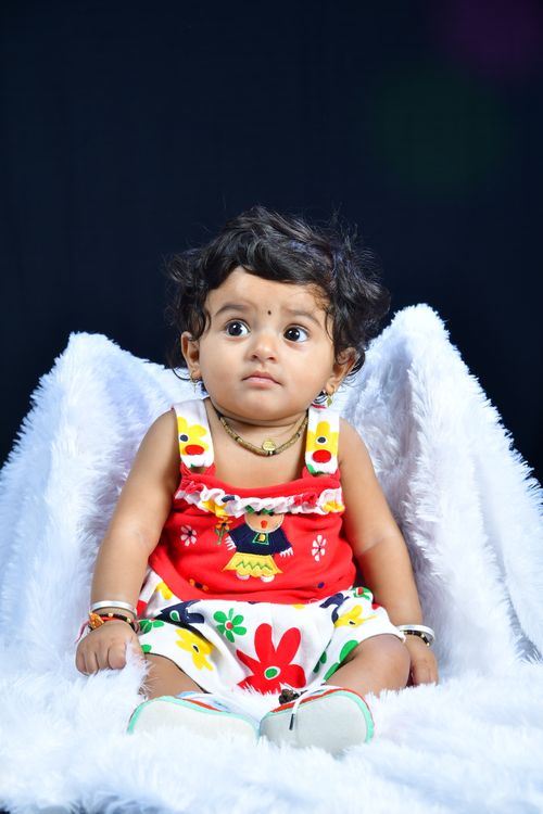 Free Cute baby girl in colorful floral dress sitting on a white fluffy blanket. Stock Photo