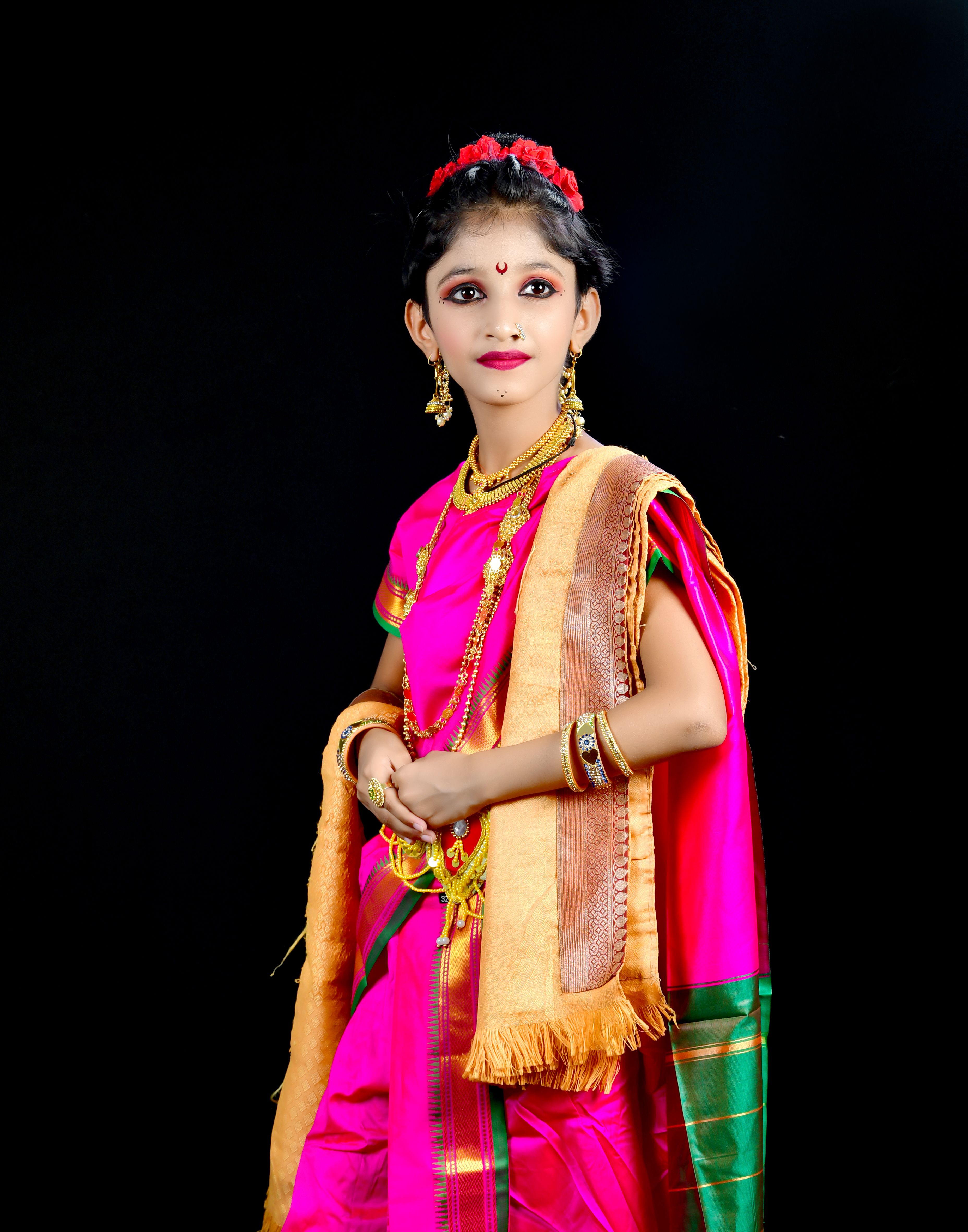 Portrait of a South Asian girl in a vibrant pink saree with jewelry against a black background.