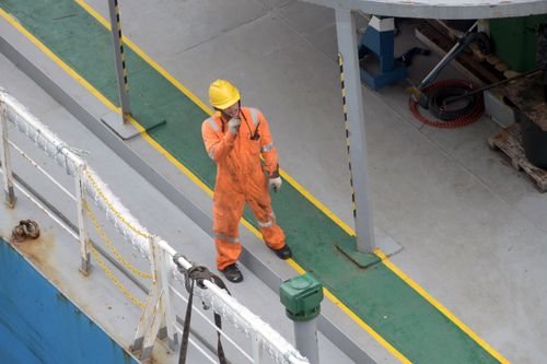 Free Overhead view of a worker in safety gear on a ship deck, showcasing industry standards. Stock Photo