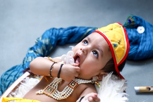 Cute baby dressed in traditional Indian clothing lying down, wearing jewelry and a vibrant hat.