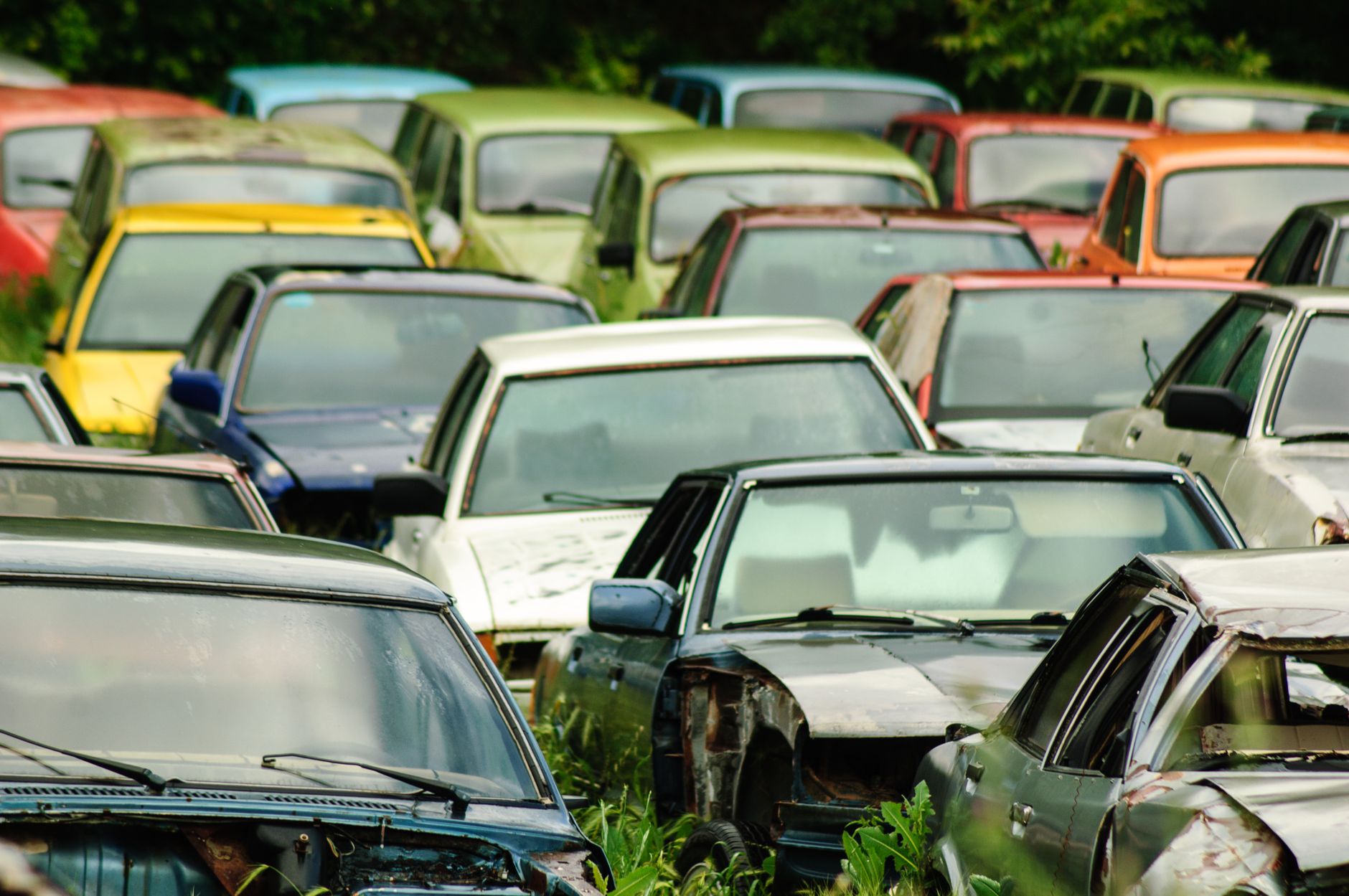 A collection of colorful vintage cars abandoned in a rural field, showcasing decay and history.