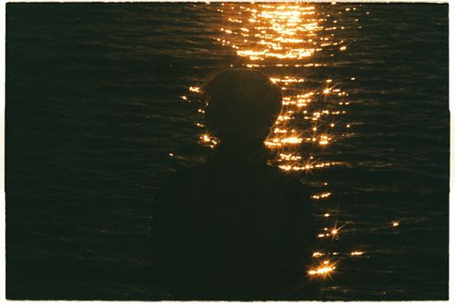 Free Silhouette of a person at the shore with golden sunset reflections on the sea surface. Stock Photo
