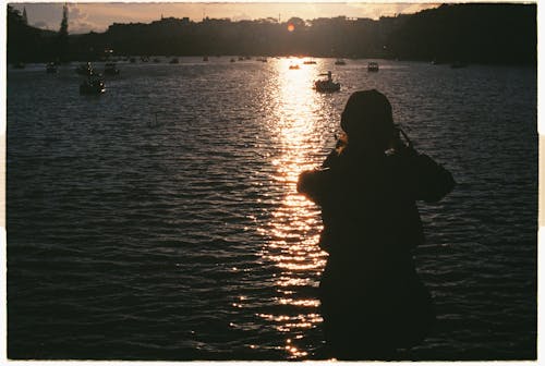 Silhouette of a Person Standing in front of a Body of Water at Sunset