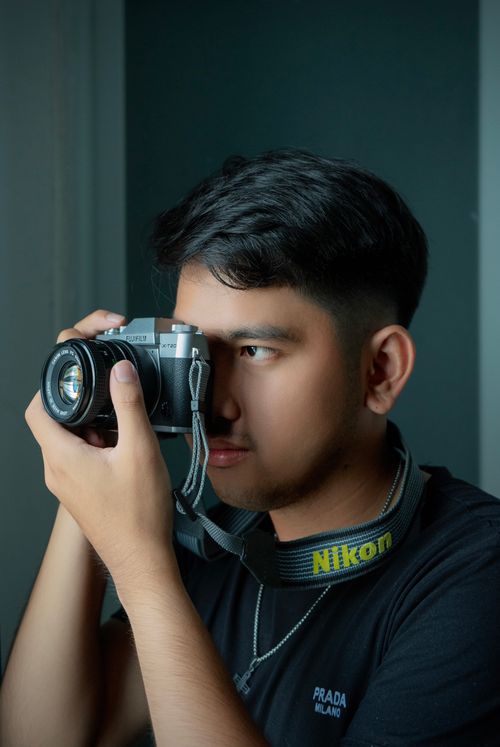 Free Portrait of a young man holding a vintage camera, focused on taking a photograph indoors. Stock Photo
