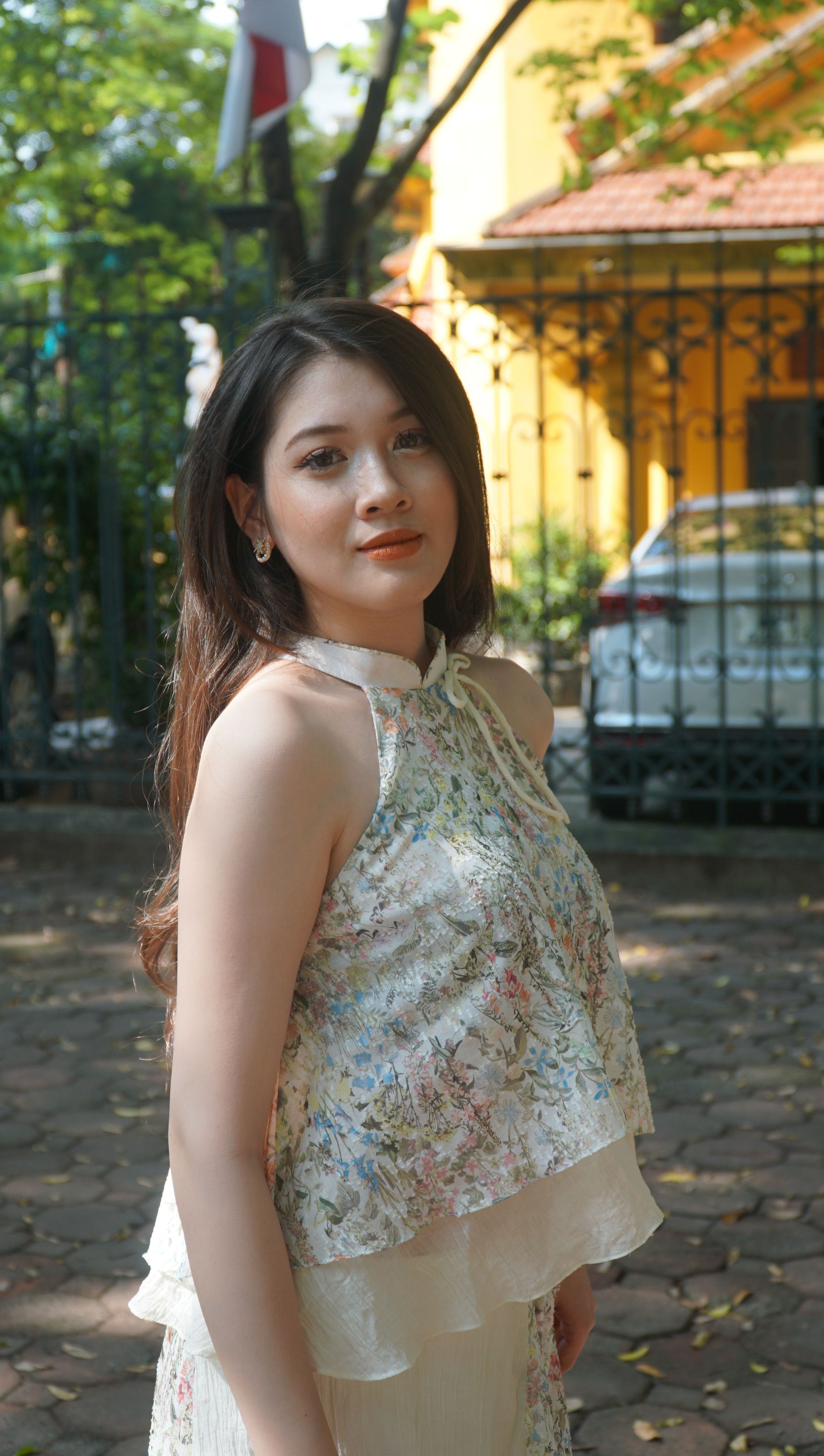Portrait of a young woman in a floral dress posing with a soft expression in an outdoor park setting.
