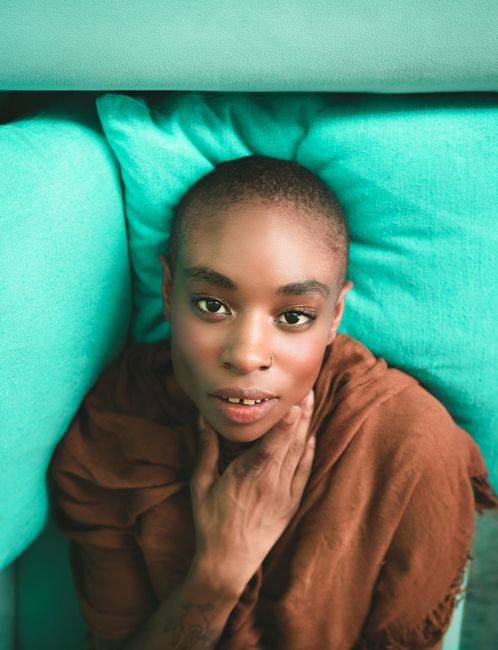 Elegant portrait of a bald woman with a captivating gaze, lying on soft cushions indoors.