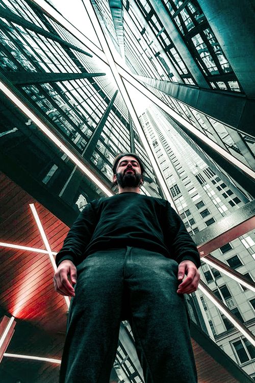 Free Dramatic low angle shot of a bearded man standing amidst towering skyscrapers in an urban environment. Stock Photo
