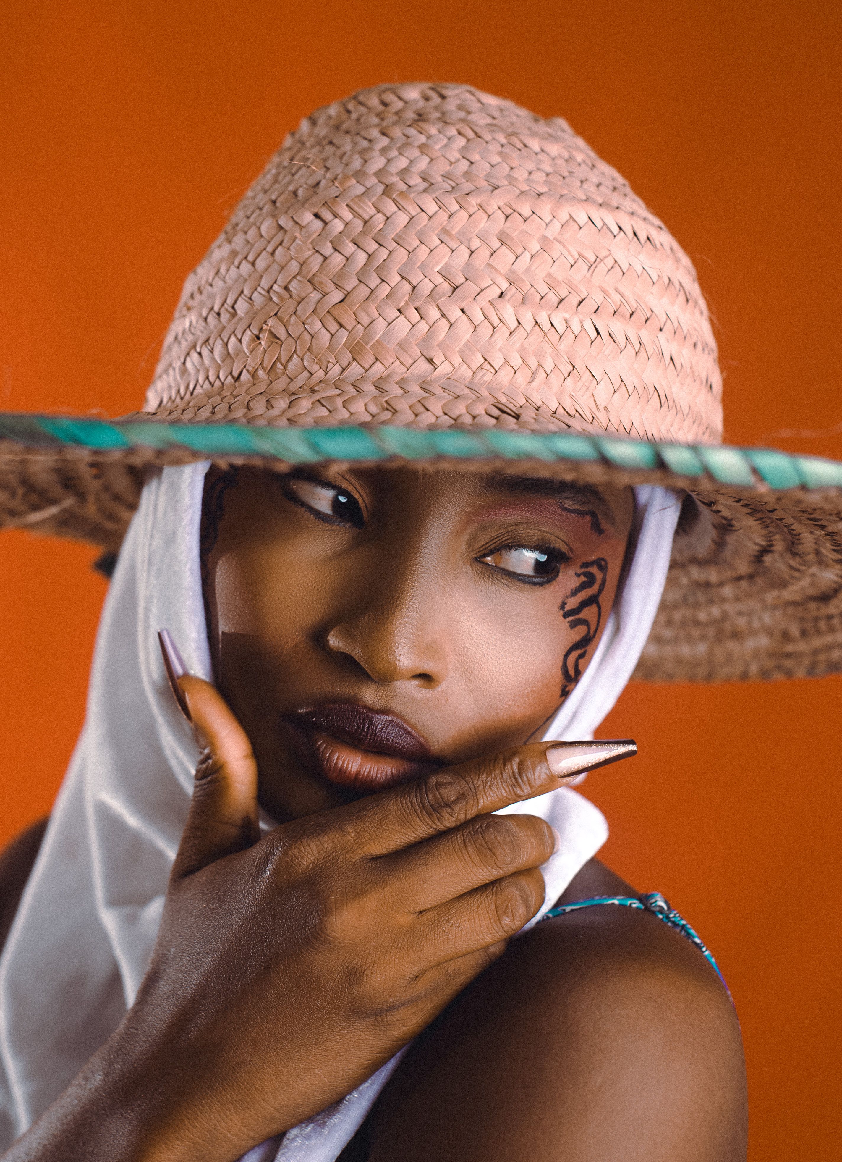 Stunning portrait of a fashionable woman in a straw hat with artistic makeup against a red background.