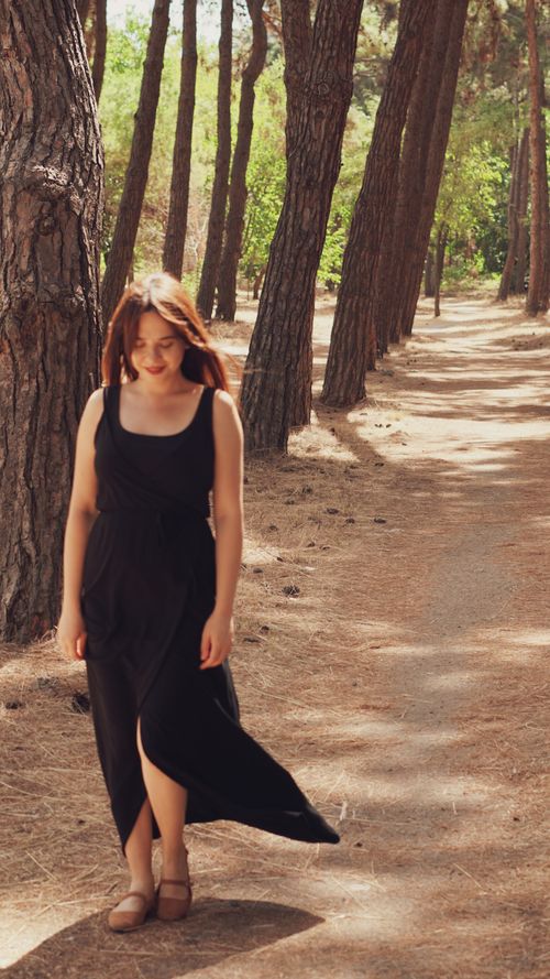 Free A woman in a flowing dress walks gracefully along a sun-dappled forest path. Stock Photo