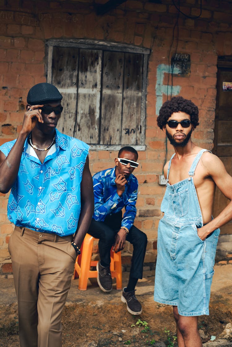 Men In Sunglasses Standing And Sitting By House In Village