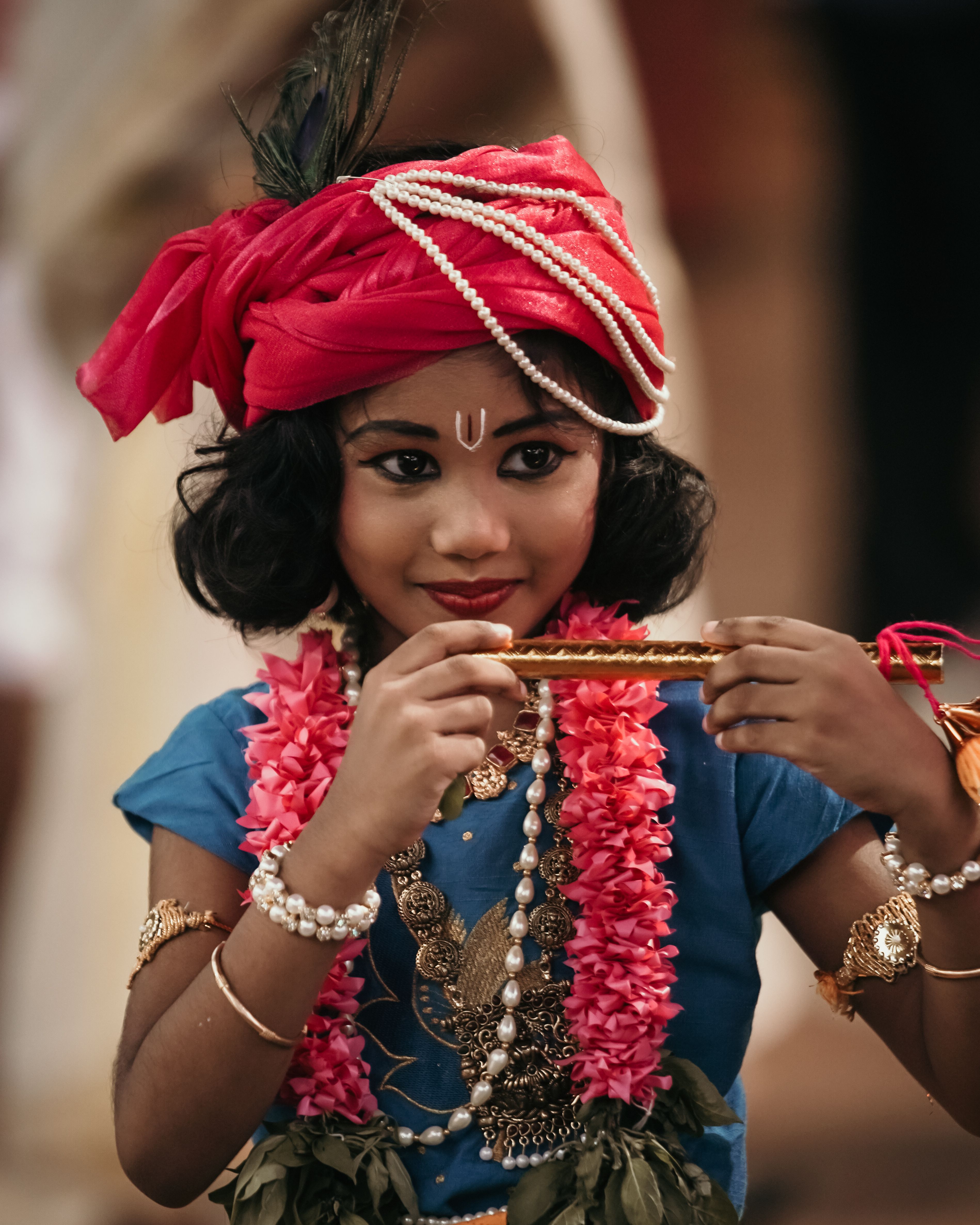 A child dressed in traditional Indian attire holding a flute, adorned with garlands and jewelry.