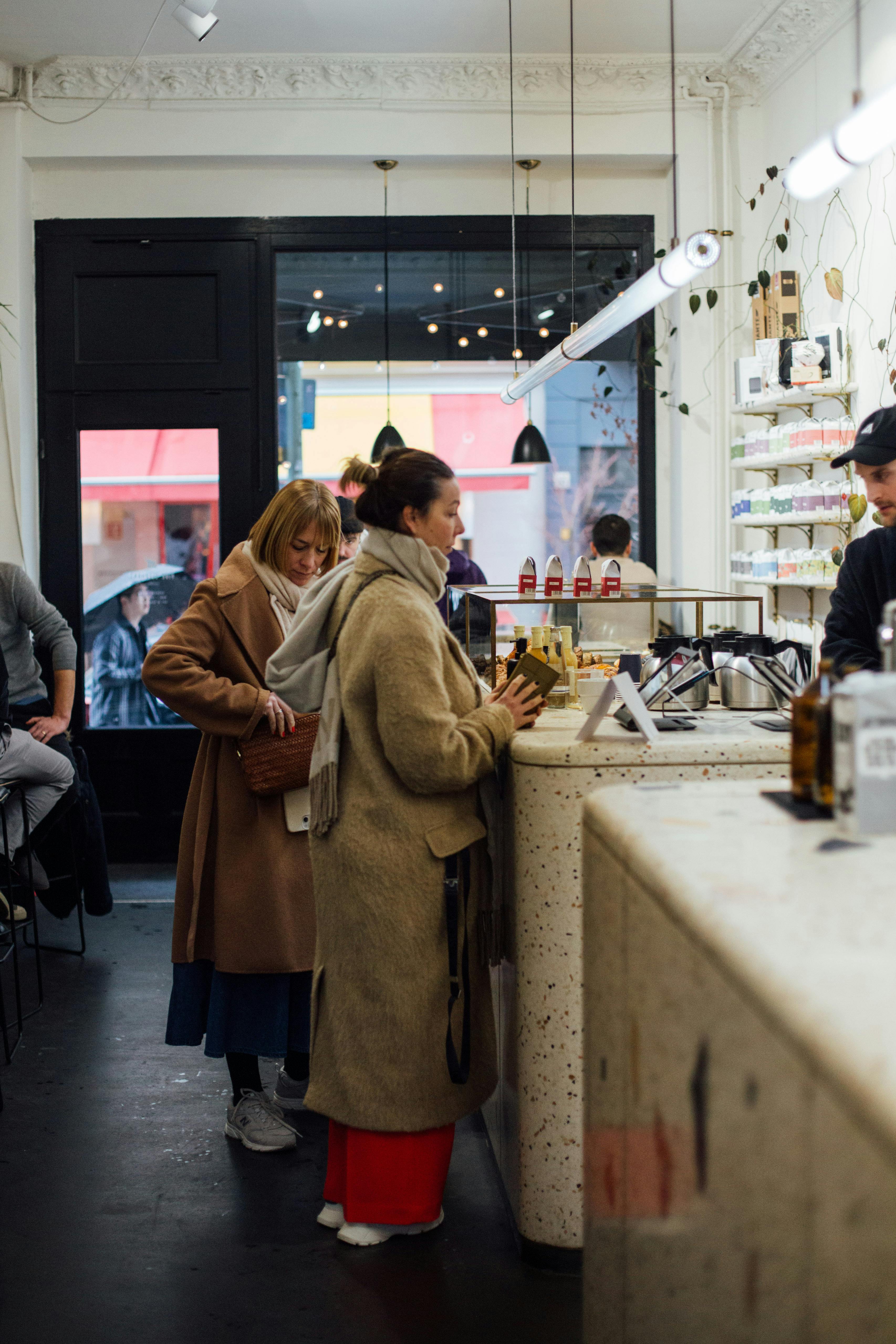Women in warm coats ordering at a stylish café counter in Berlin, Germany.
